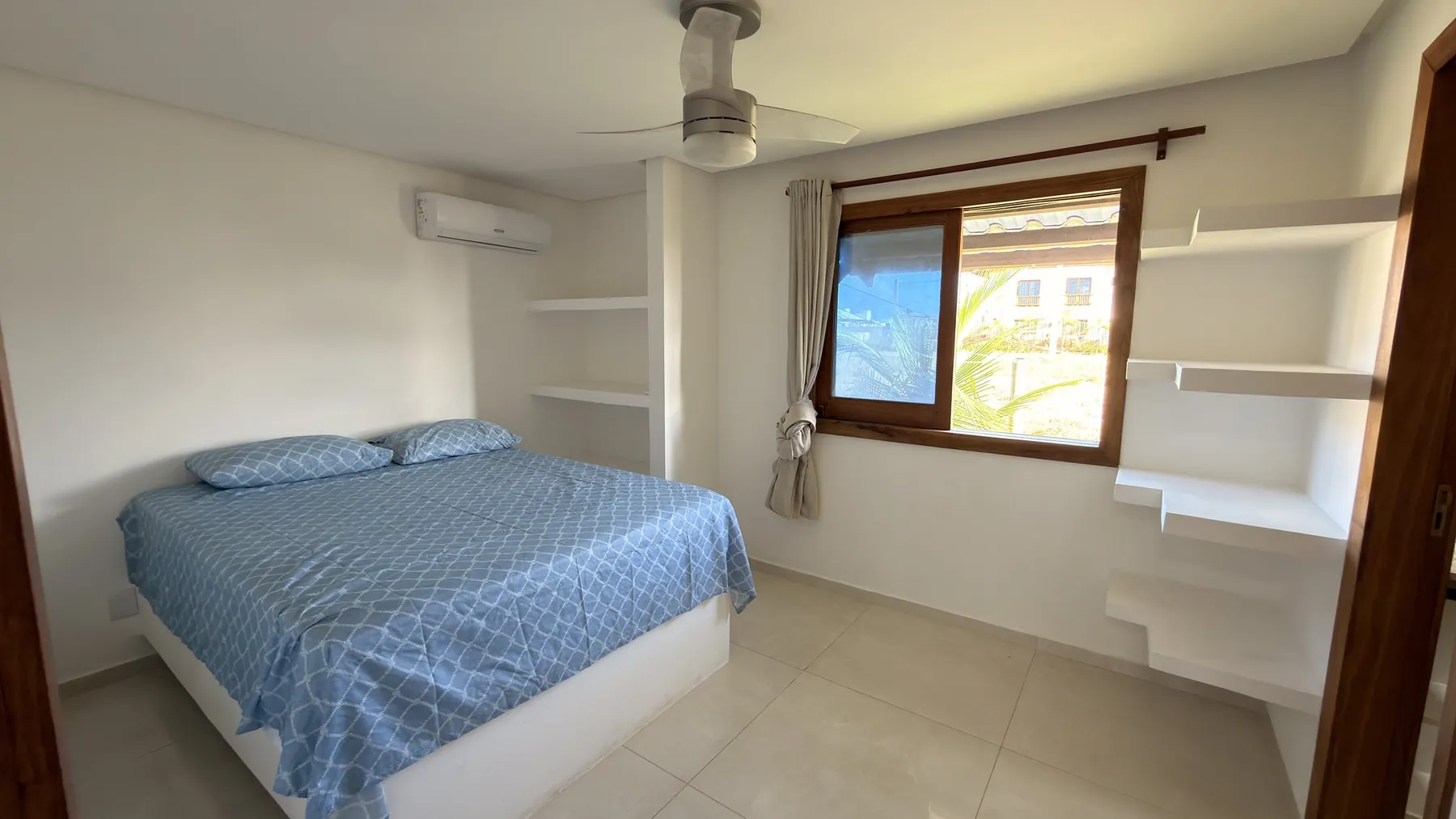 Quarto da casa com cama de casal, ar-condicionado e janela de madeira