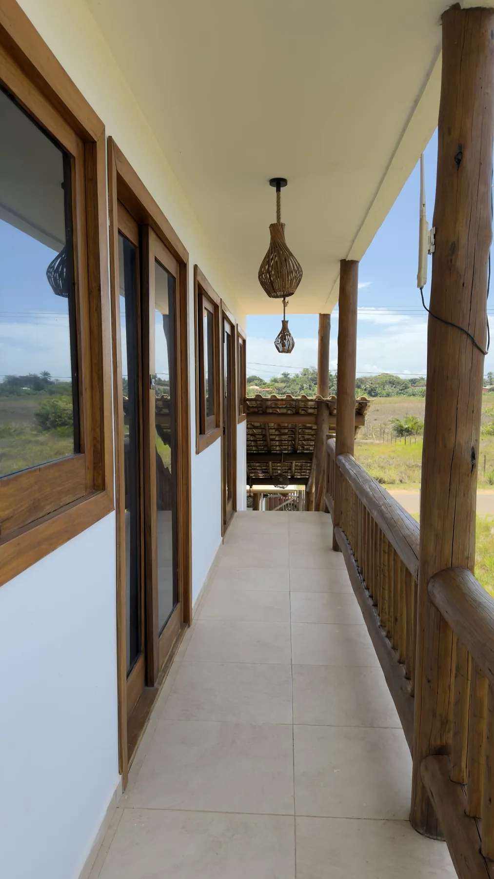 Varanda dos flats com pendente de fibra natural e vista para o campo