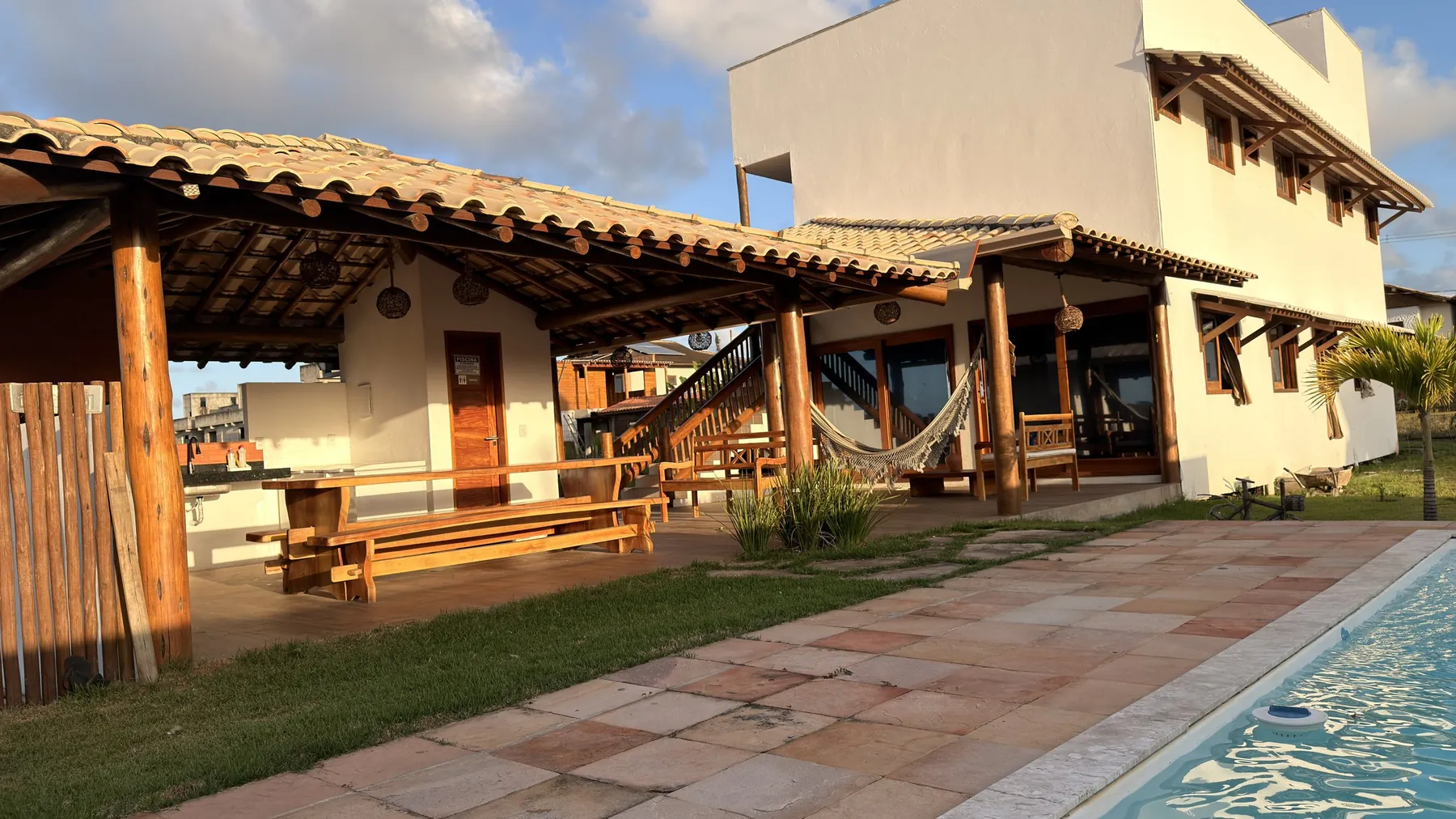Área coberta com telhado colonial e a casa ao fundo, vistas da beira da piscina