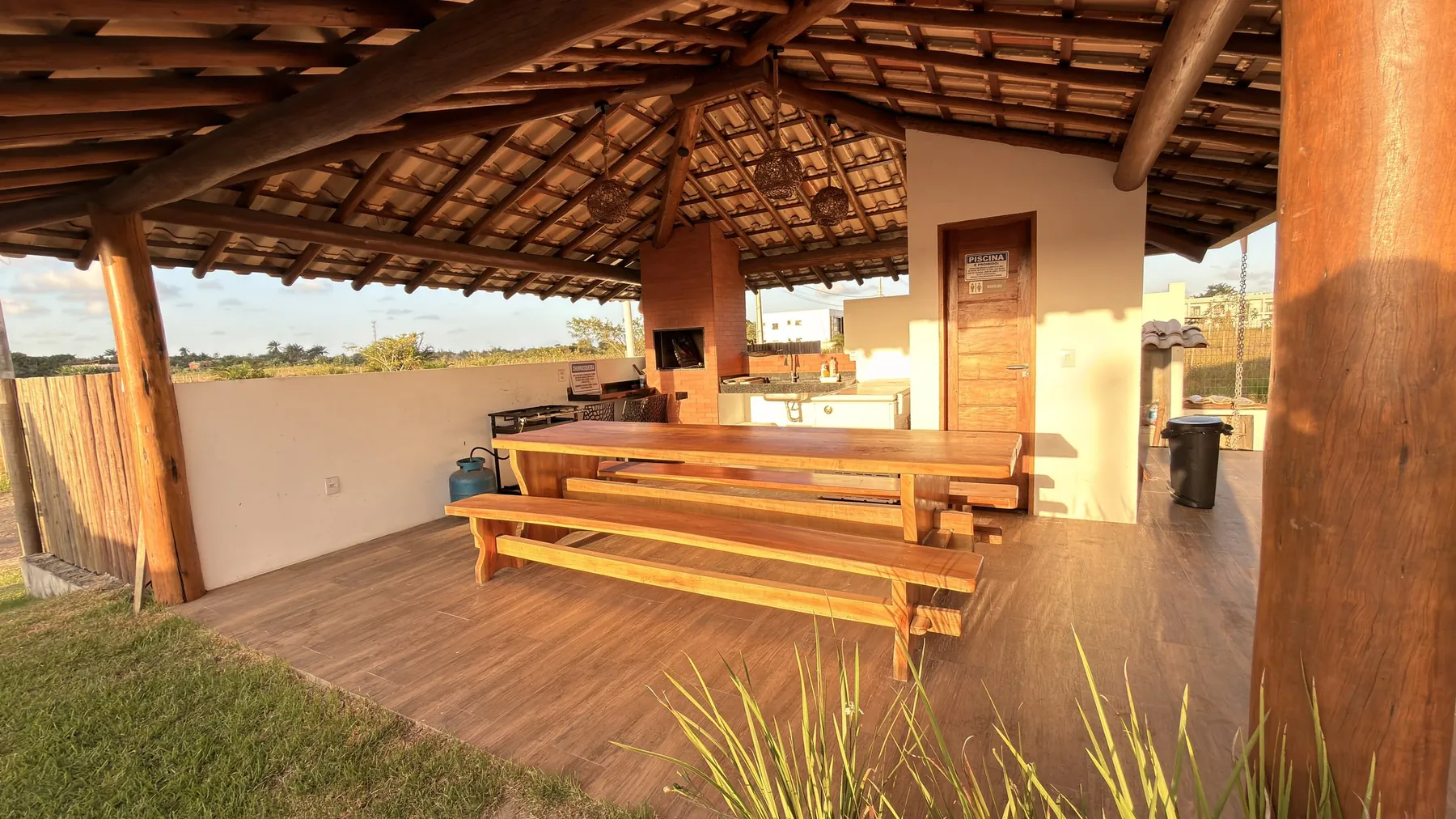 Mesa comprida de madeira na área gourmet, com gramado ao redor